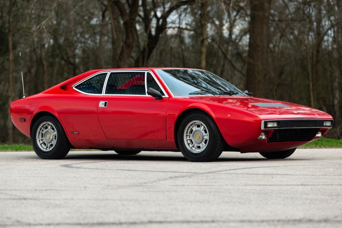 A profile view of a red Ferrari 308 GT4 parked with trees in the background
