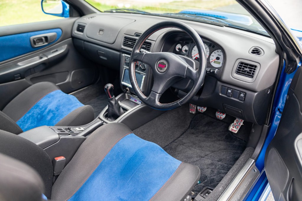 The black dashboard and blue-and-black front seats of a blue 1998 Subaru Impreza 22B STi