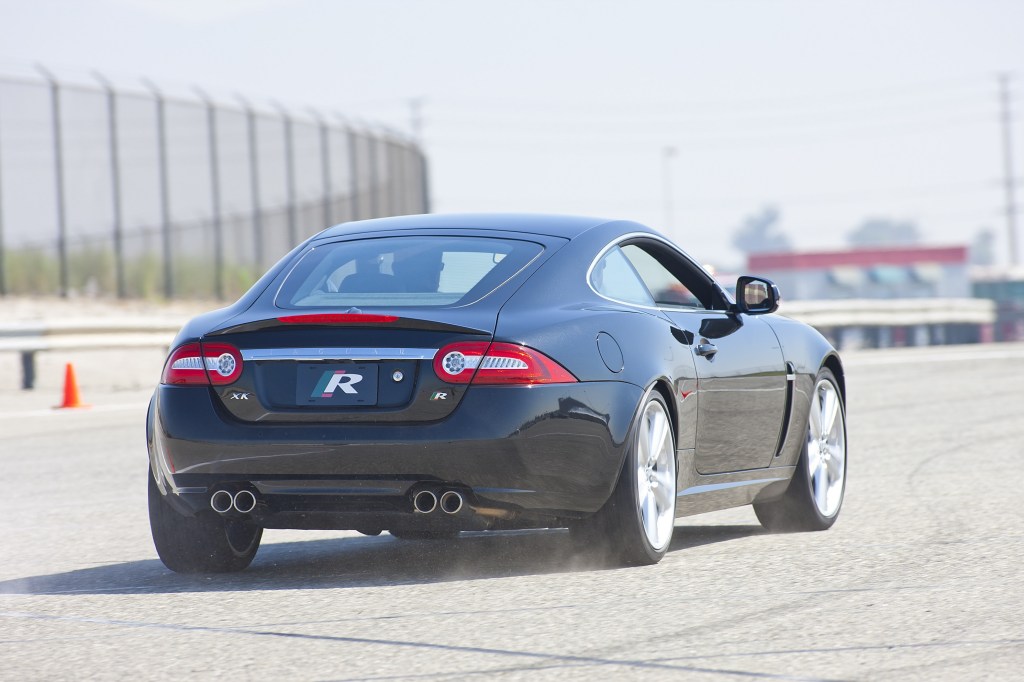 The rear 3/4 view of a black 2011 Jaguar XKR Coupe on a racetrack