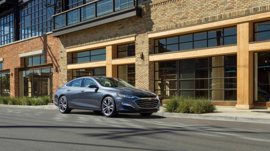 The 2021 Chevrolet Malibu midsized sedan parked outside a wood and brick building