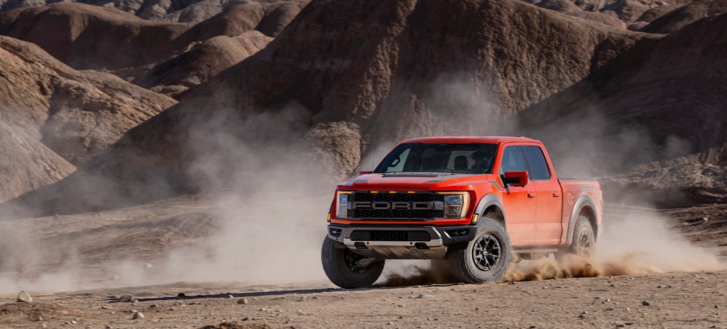 Red Ford F-150 raptor supertruck skidding through the desert with hills in the background.