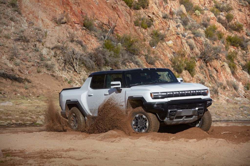 The new Hummer EV truck using its 1,000 horsepower and giant 35-inch tires to turn its wheels in the sand. 
