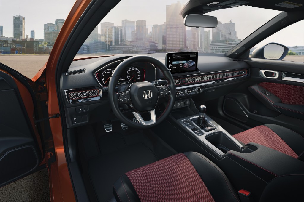 The red-and-black front sport seats and black dashboard of an orange 2022 Honda Civic Si