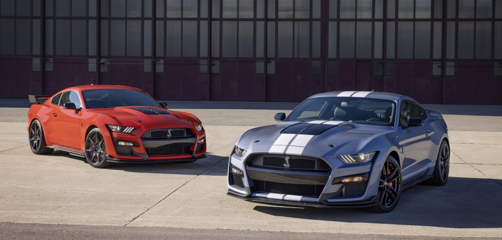 An orange 2022 Shelby GT500 with Carbon Fiber Track Package next to a blue and white 2022 Shelby GT500 Heritage Edition in front of a hangar