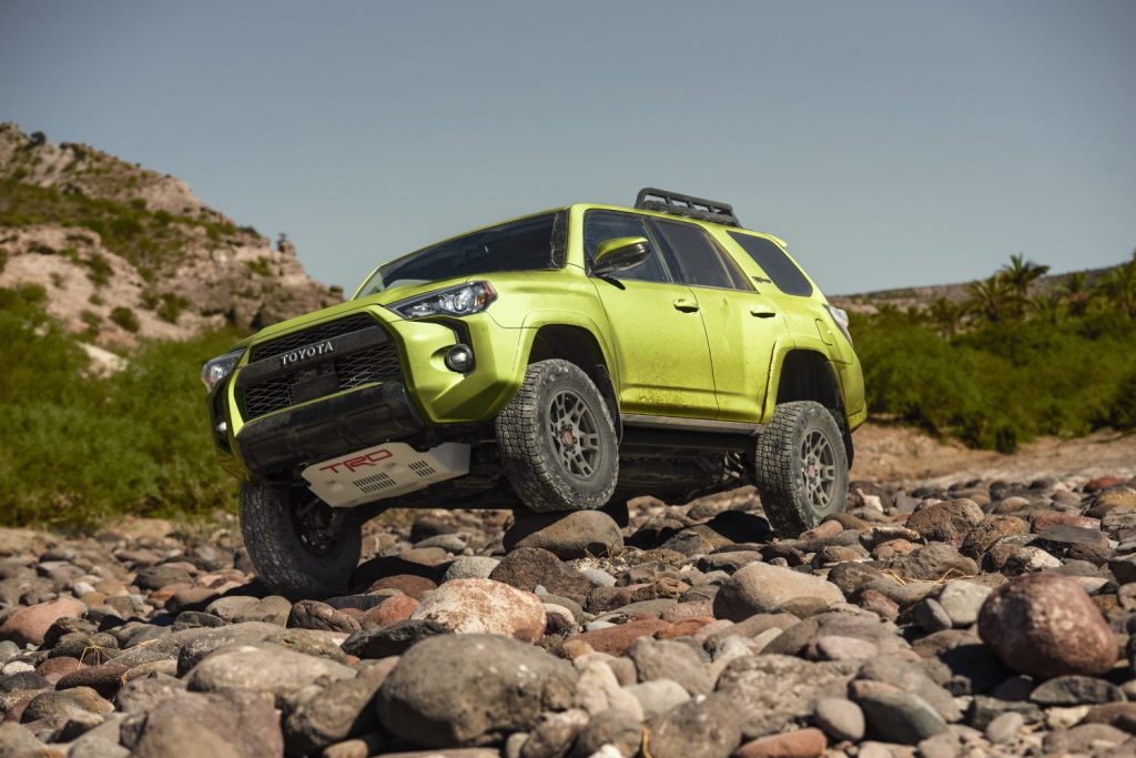 Lime green Toyota 4Runner SUV flexing its suspension to climb over boulders, its TRD Pro skid-plate clearly visible.
