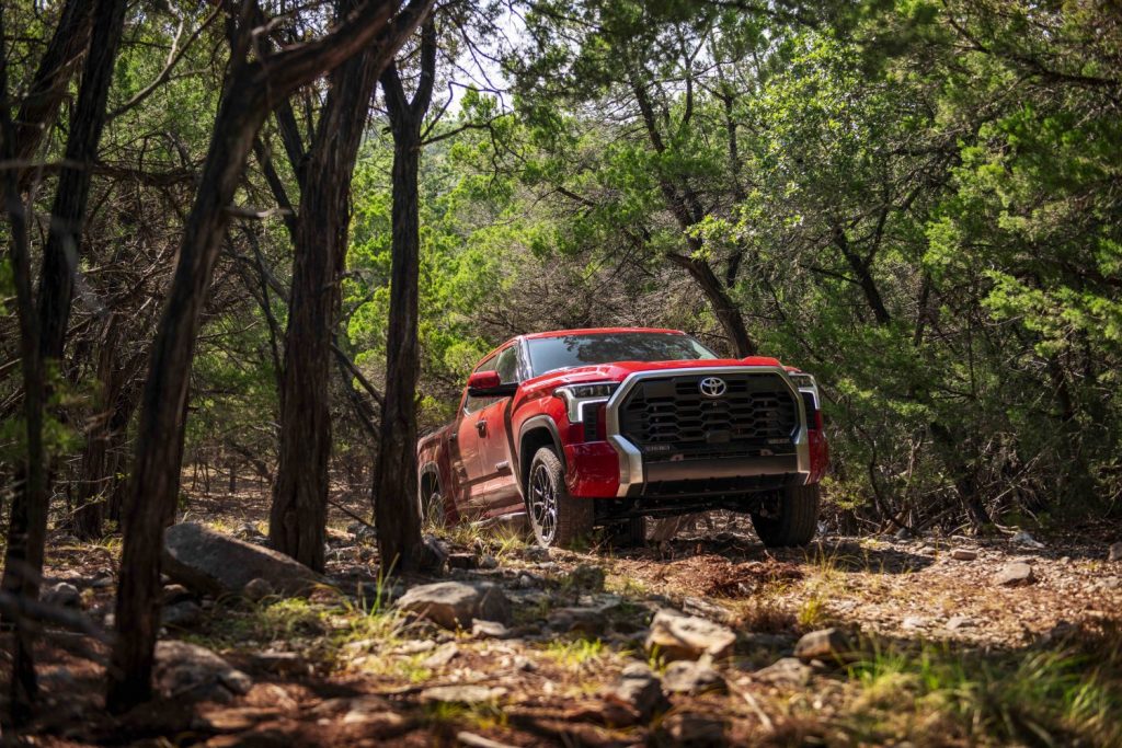 Red Toyota Tundra pickup truck cresting a hill in a wooded trail with trees visible on either side.