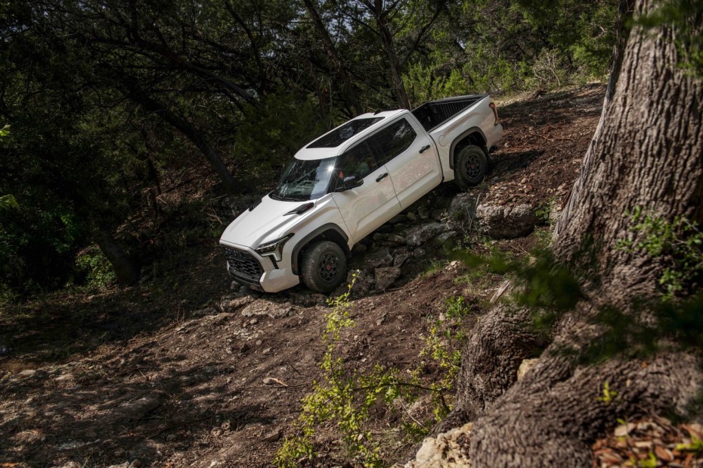 White full-size Toyota pickup truck creeping down a 45-degree pitch in a boulder-strewn off-road trail.