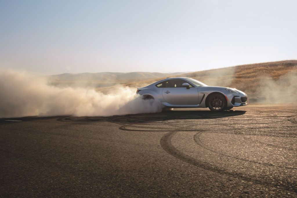 Silver 2022 Subaru BRZ drifting around a corner on a paved track, kicking up dust from its rear tires
