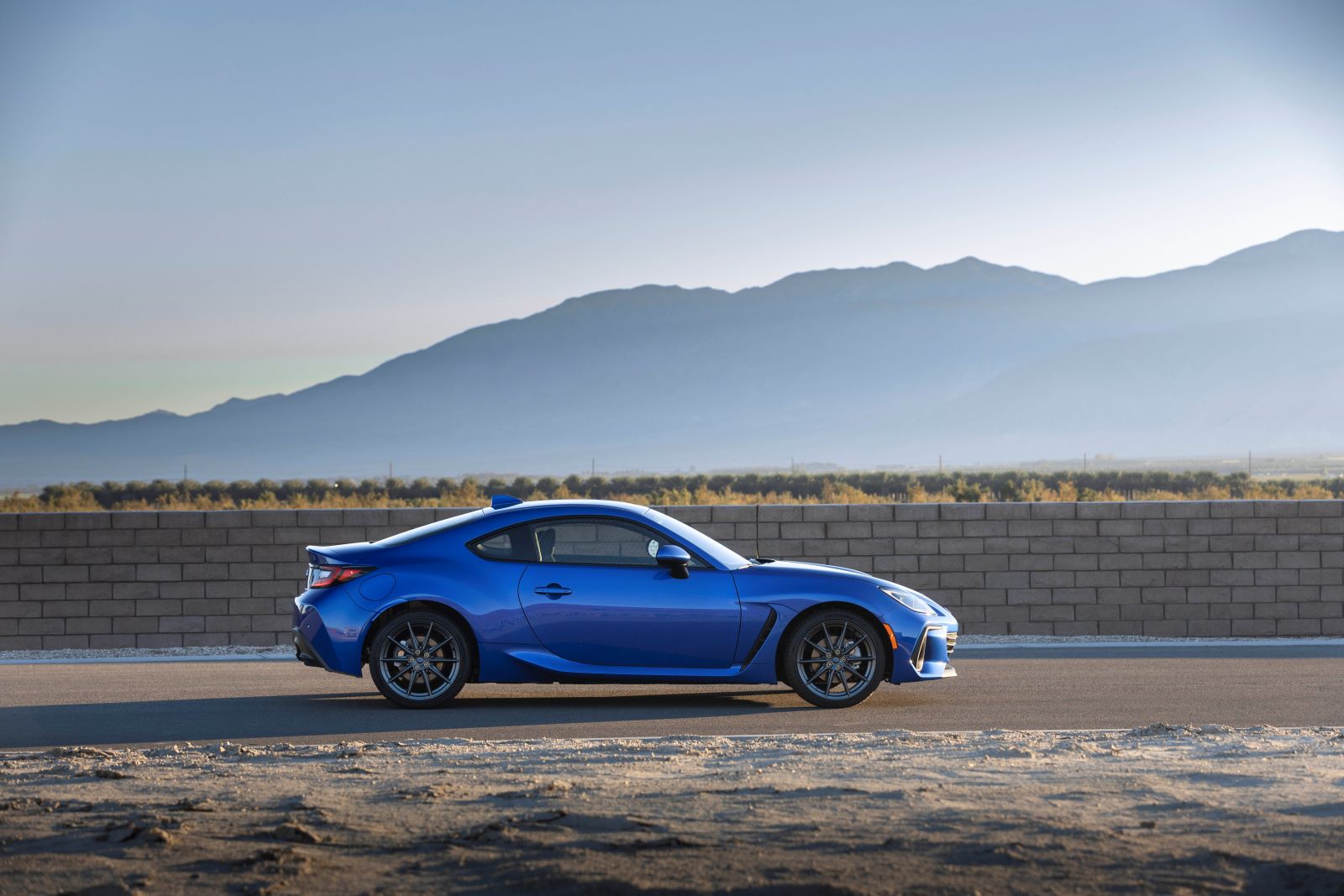 Side profile of a blue 2022 Subaru BRZ coupe, trim level uncertain, parked on a road against the backdrop of sprawling mountains