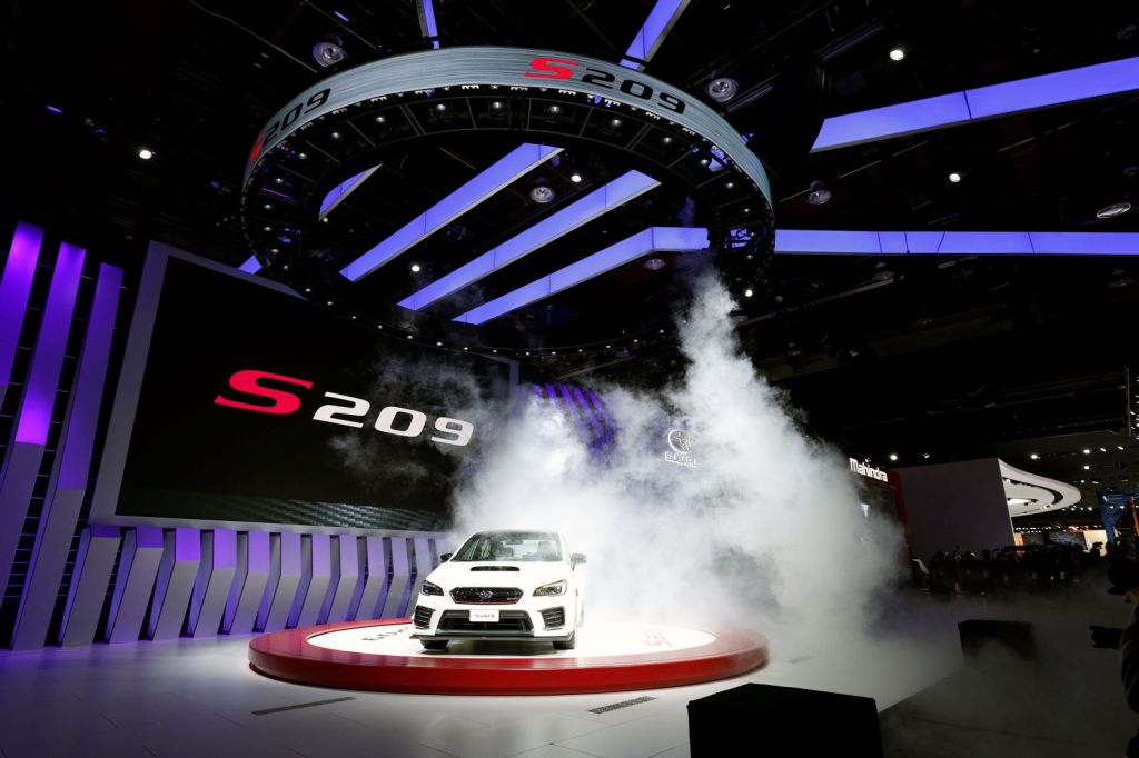 A white 2019 Subaru S209 STI sports car sits on a stage at an automotive show, with manufactured fog floating around it for dramatic effect