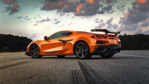 A 3/4 rear view of an orange 2023 Chevrolet Corvette Z06 parked on a road with trees in the background.