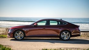 A profile view of a dark red 2022 Genesis G80 sedan parked in front of a beach.