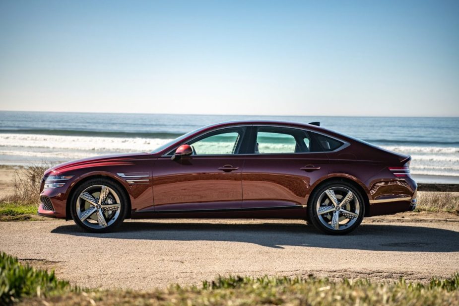 A profile view of a dark red 2022 Genesis G80 sedan parked in front of a beach.