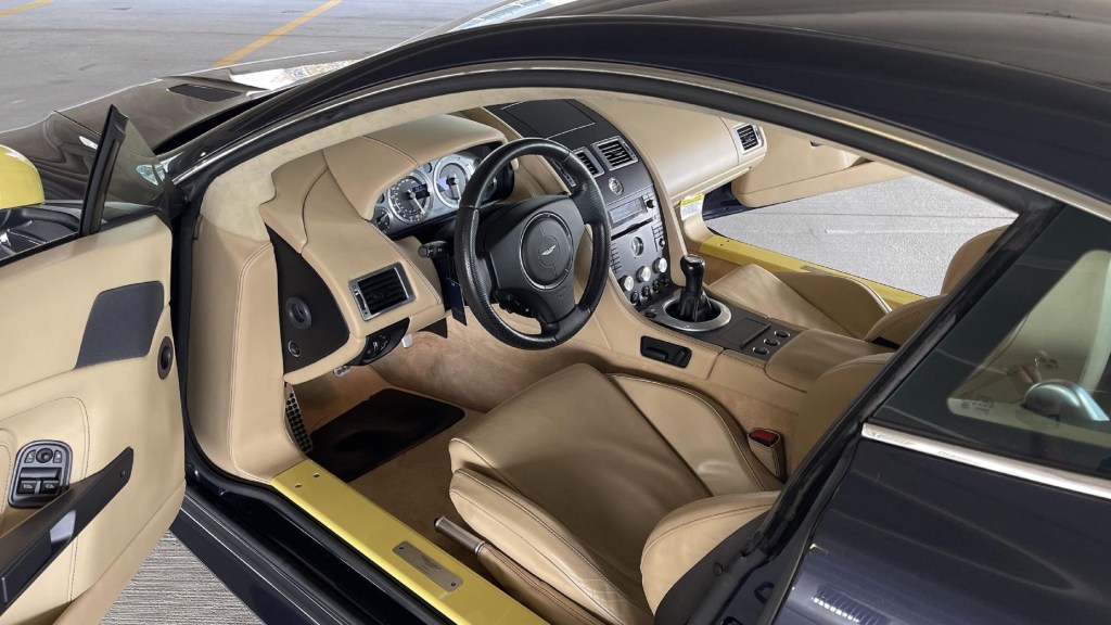 The tan-leather seats and dashboard of a blue-and-yellow modified 2006 Aston Martin V8 Vantage manual
