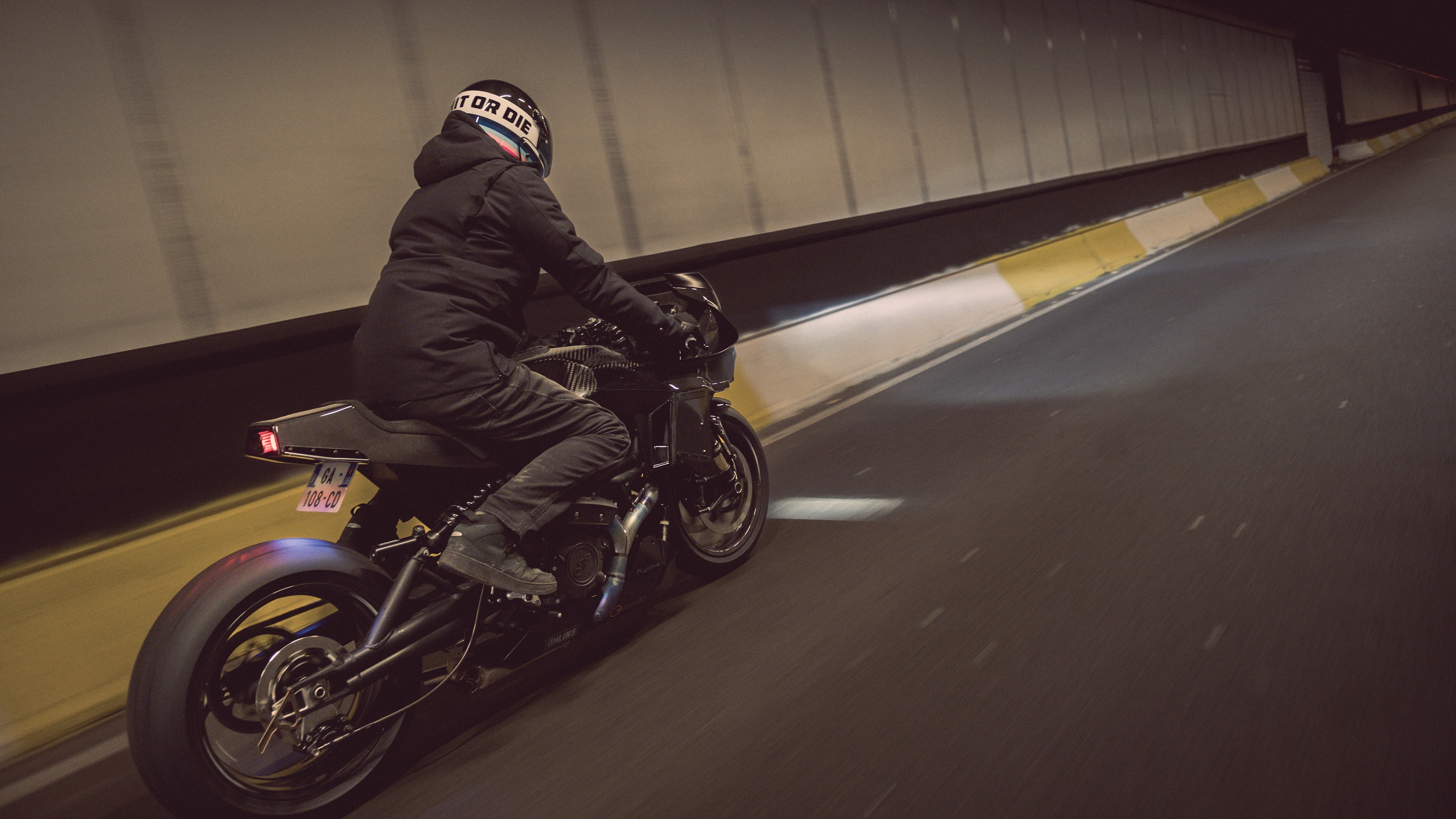 A rear 3/4 view of a black-clad rider on Workhorse Speed Shop's Indian FTR 'Black Swan' in a tunnel