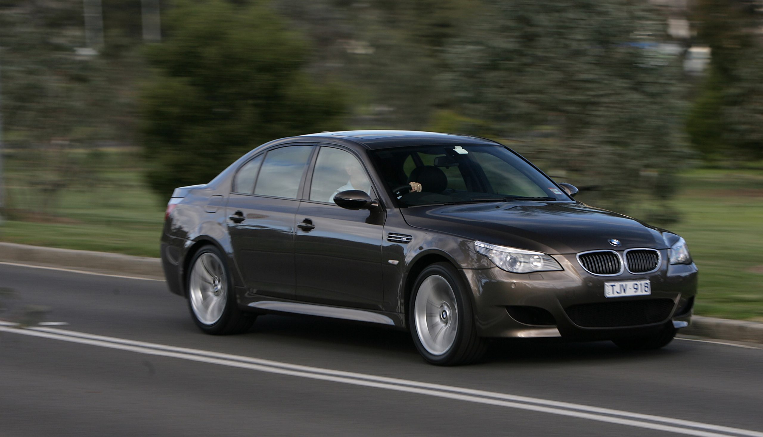 A brown 2005 E60 BMW M5 sports car driving down the road at speed