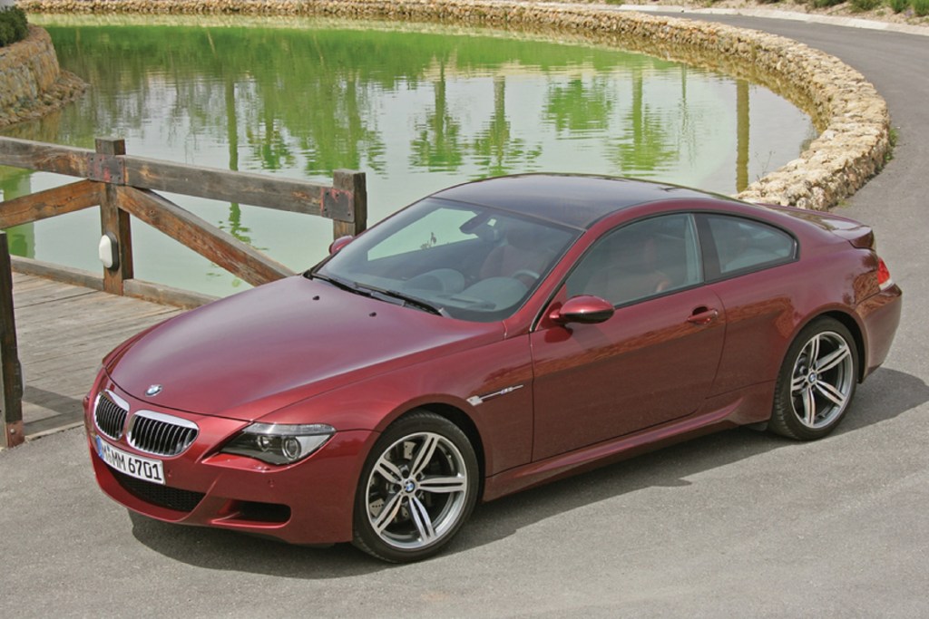 A red 2010 E63 BMW M6 sports car parked by a pond
