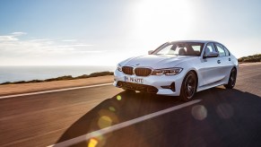 White 2022 BMW 330e plug-in hybrid sedan driving down coastal highway at sunset