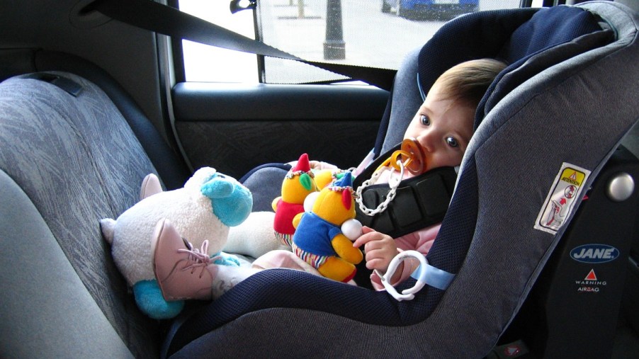 Baby sitting in a child seat in a car, highlighting locksmith program that opens locks for free to save kids and pets
