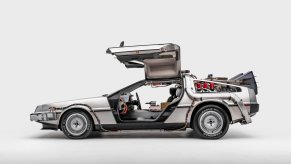 A profile view of the 1981 DeLorean Time Machine from the movie Back to the Future. Car is displayed in a white studio background with the doors open.