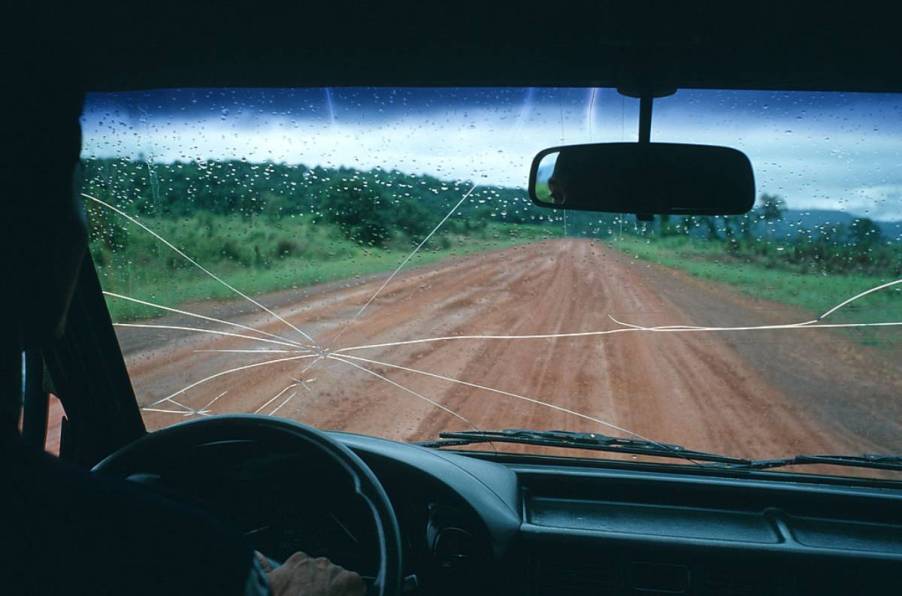 A car driving down a dirt road with a cracked windshield.