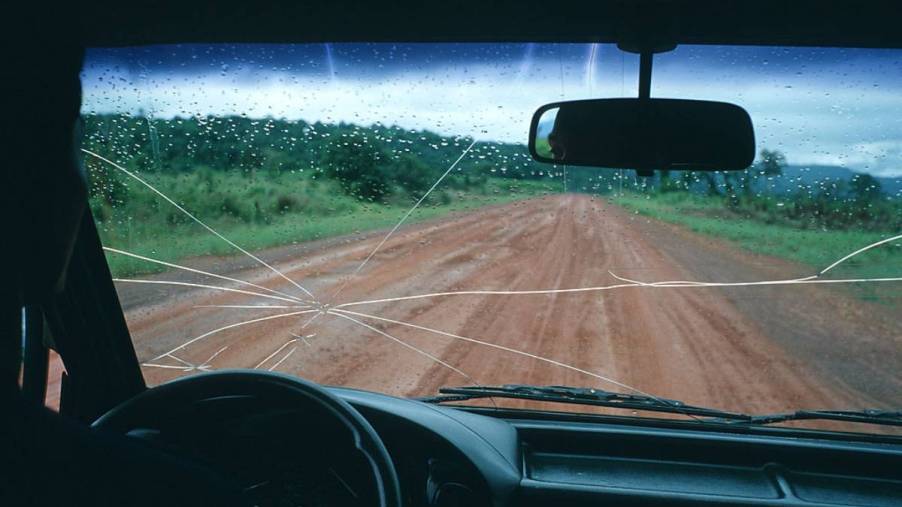 A car driving down a dirt road with a cracked windshield.
