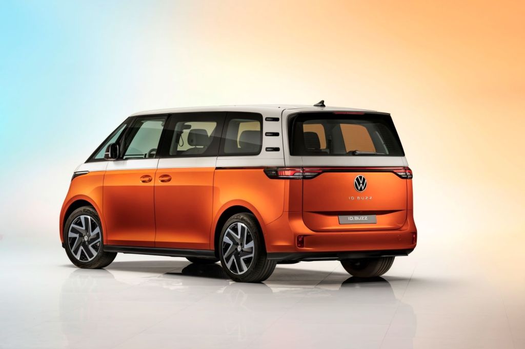 Driver's side rear angle view of orange and white 2024 VW ID. Buzz, highlighting its release date and price