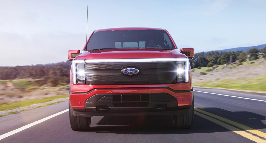 A red 2022 Ford F-150 Lightning electric pickup truck is driving down the road.
