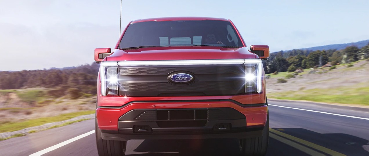 A red 2022 Ford F-150 Lightning is driving down the road.