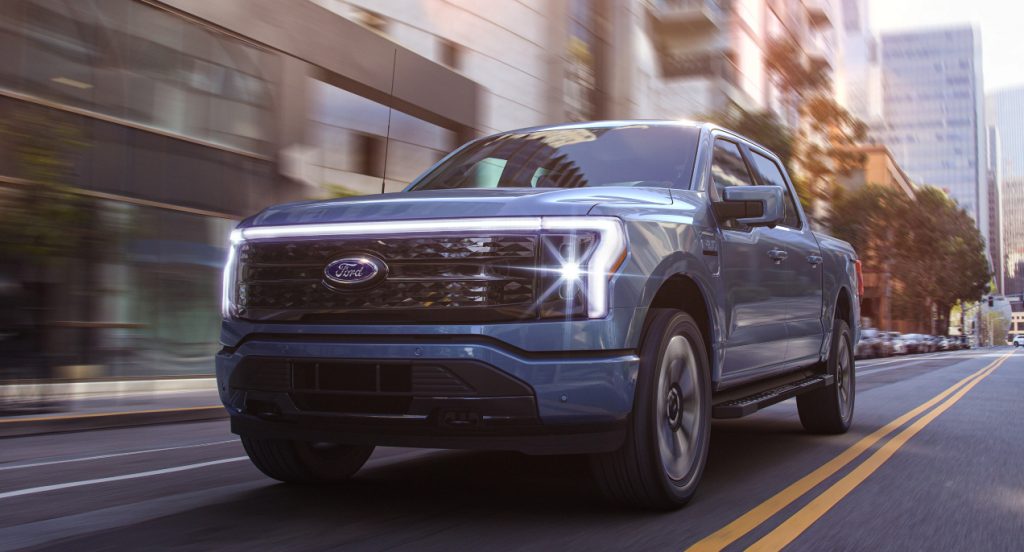 A blue 2022 Ford F-150 Lightning electric pickup truck drives down the road.