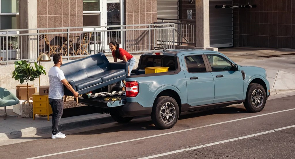 A blue 2022 Ford Maverick is parked while people load furniture. 