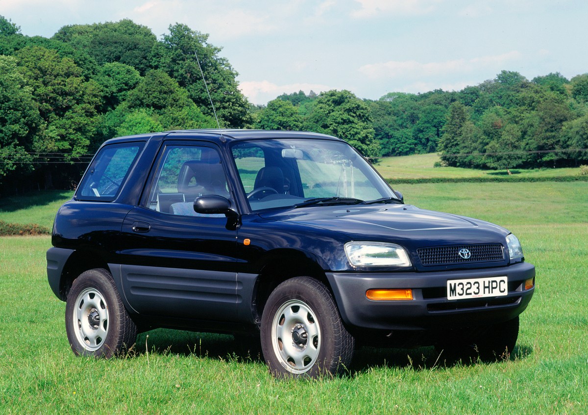 A 3/4 front view of a black 1995 Toyota RAV4 crossover SUV parked in a grassy field with trees in the far background.