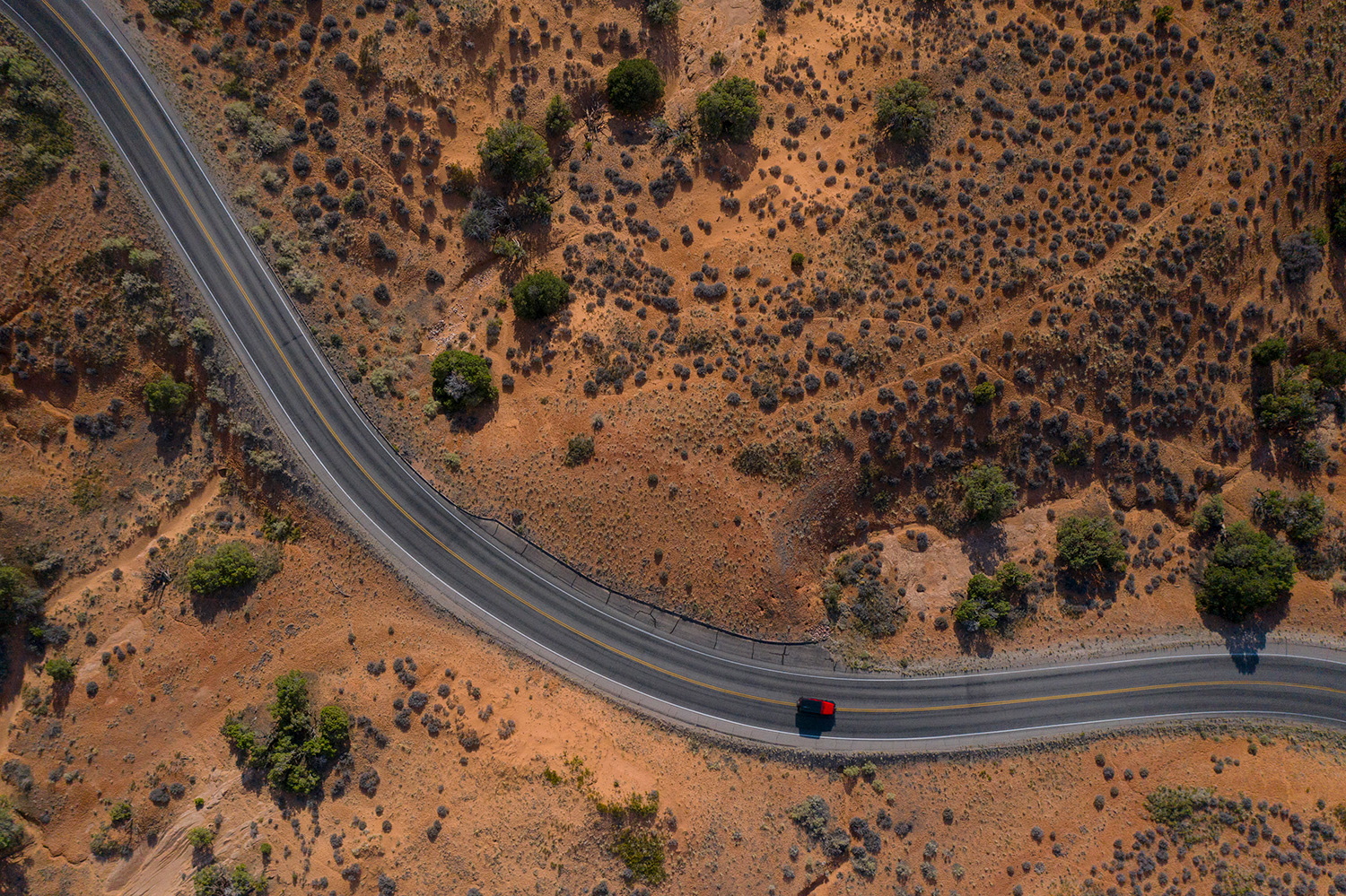 Drone aerial view of winding road and red car in Utah.