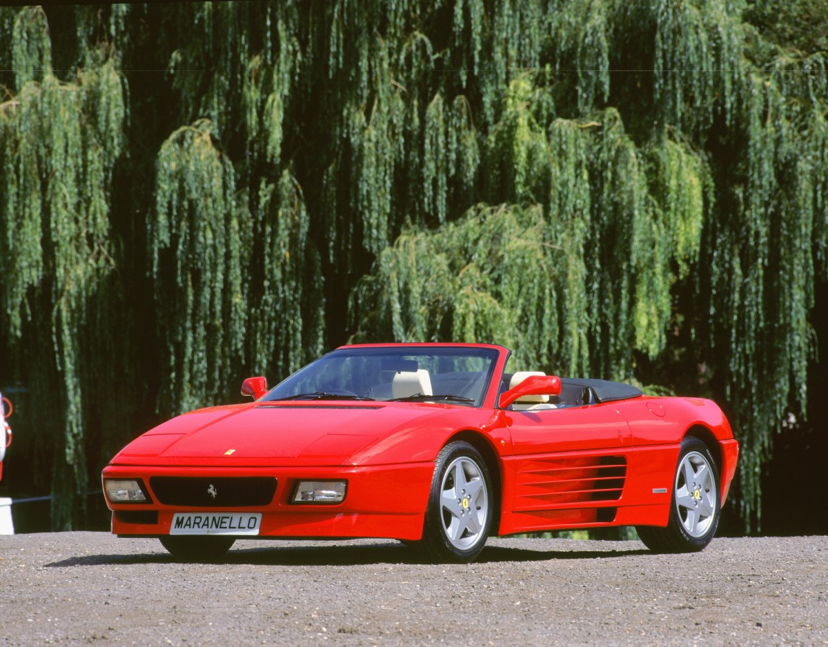 A 3/4 front view of a red 1993 Ferrari 348 Spider parked in front of a large tree