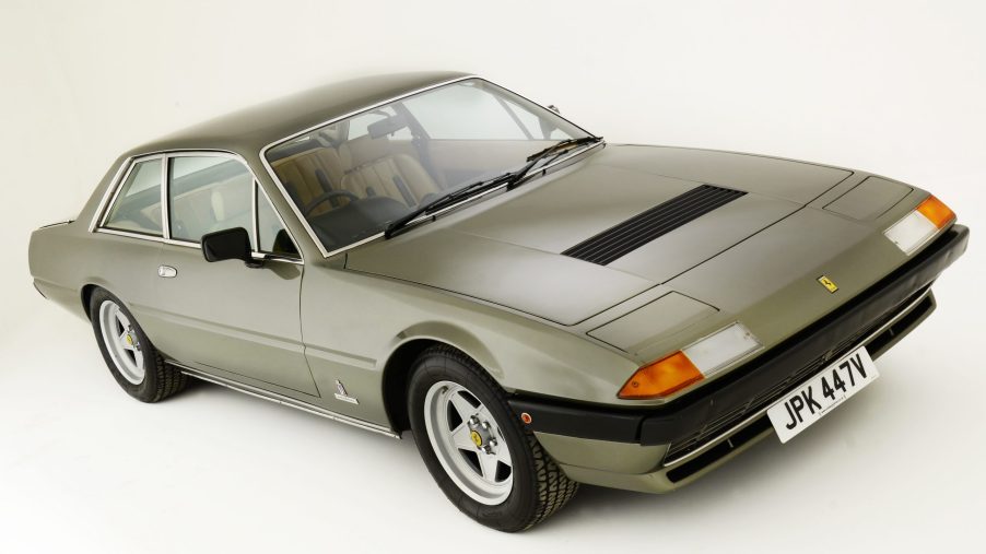 A 3/4 front and overhead view of a light brown 1980 Ferrari 400i with a white studio background