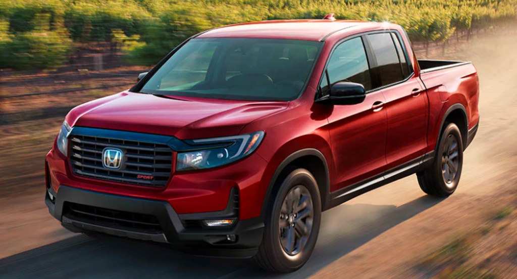 A red 2022 Honda Ridgeline midsize pickup truck is driving off-road. 