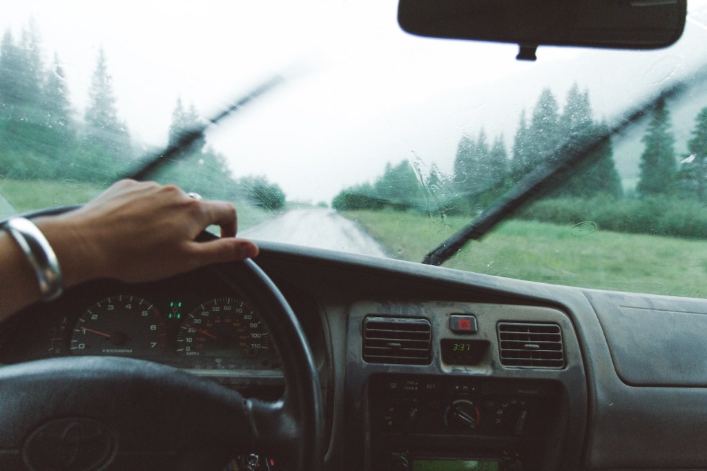 The dashboard of a driving car, its windshield wipers a blur in the background.