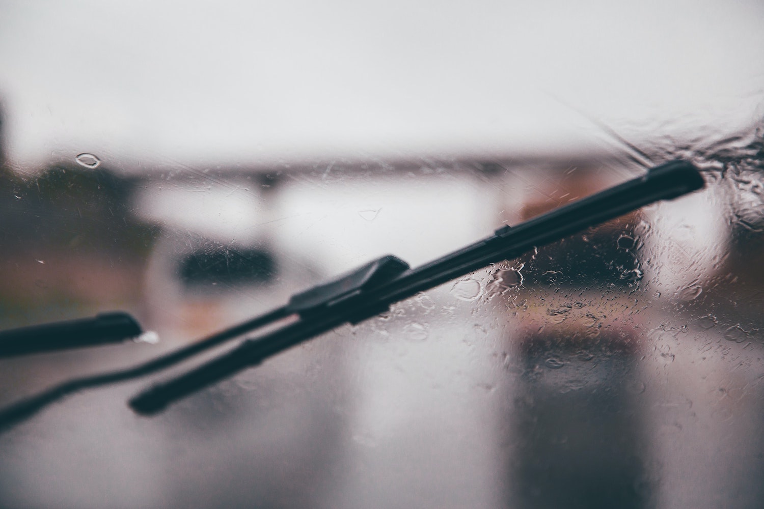 Wipers cleaning a wet windshield, a rainy road visible in the background.