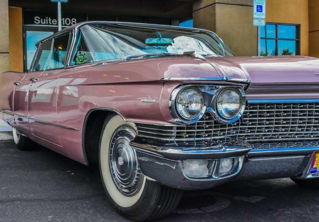 Closeup of the headlights of a large, pink, classic car.