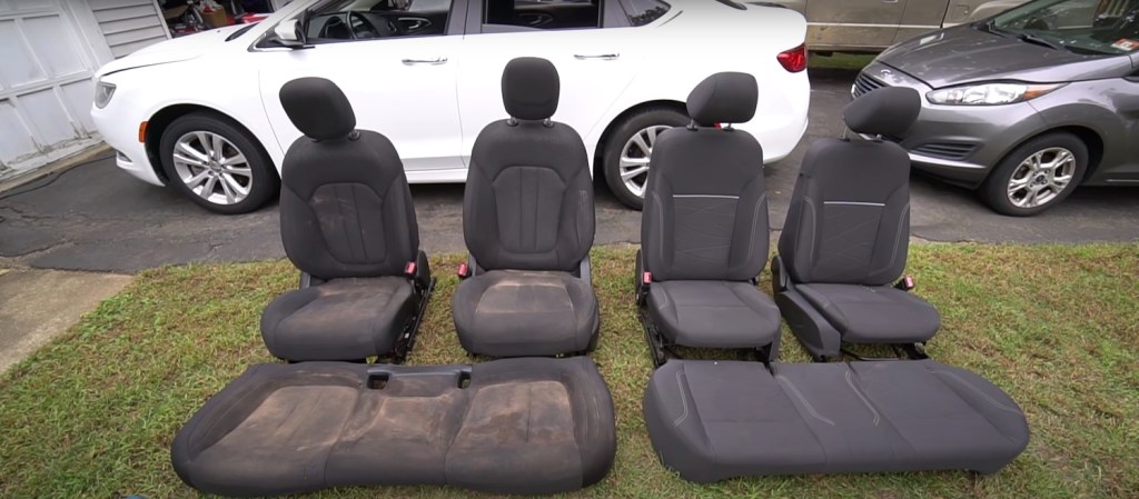 Car seats in the midst of a cleaning, sitting on a lawn in front of a car.