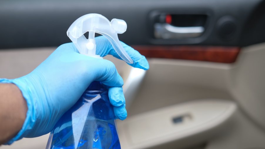 An automotive detailer's hand spraying a car interior with a cleaner.