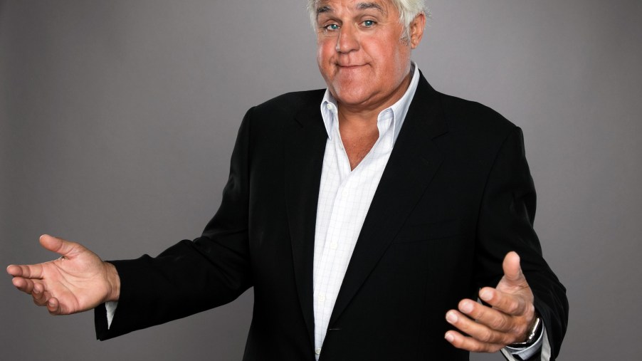 Jay Leno shrugs and smiles, wearing a suit, in a publicity photo.