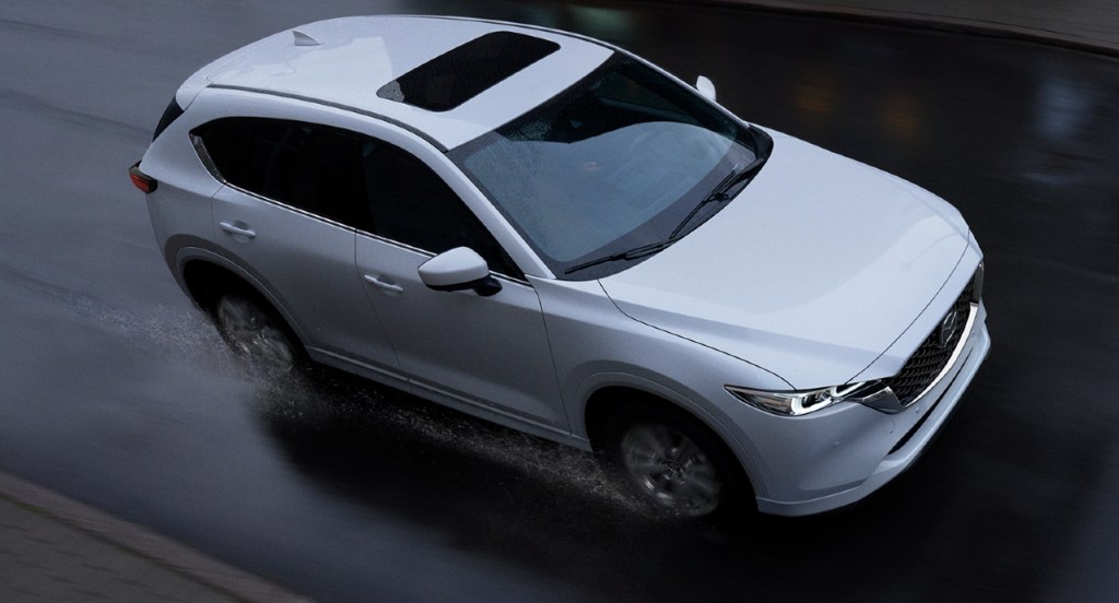 A white 2022 Mazda CX-5 small SUV is driving in the rain. 