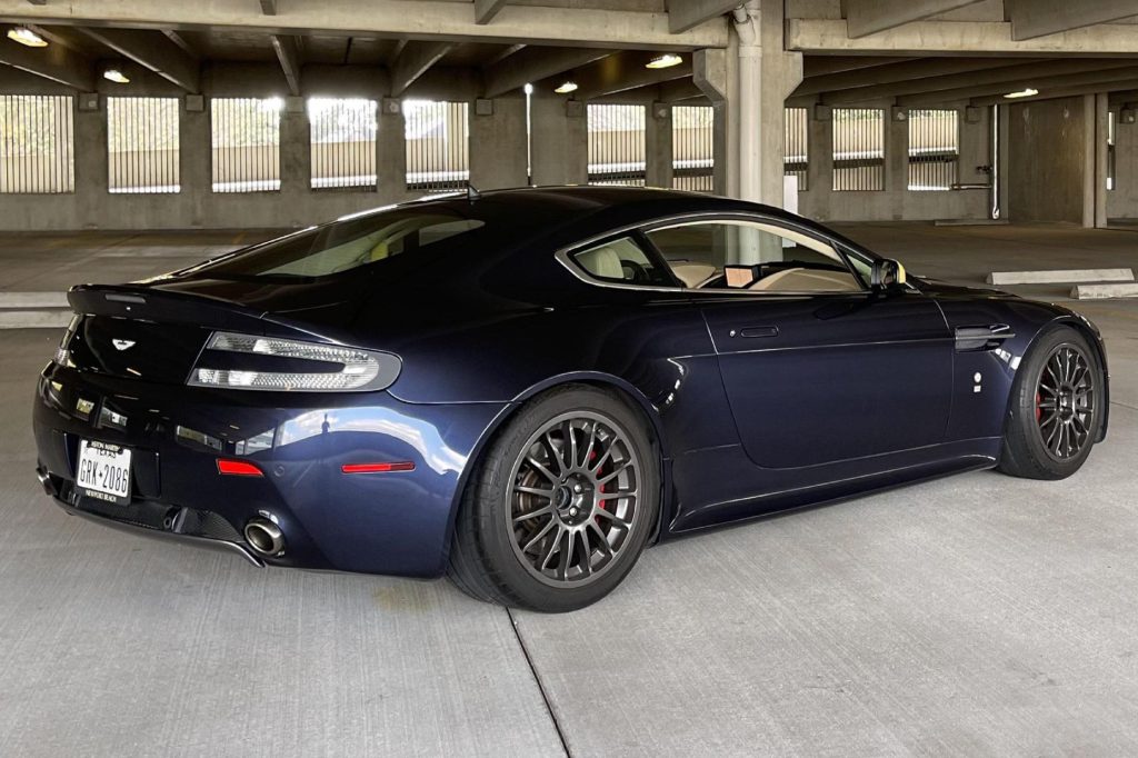 The rear 3/4 view of a blue-and-yellow modified 2006 Aston Martin V8 Vantage in a parking garage