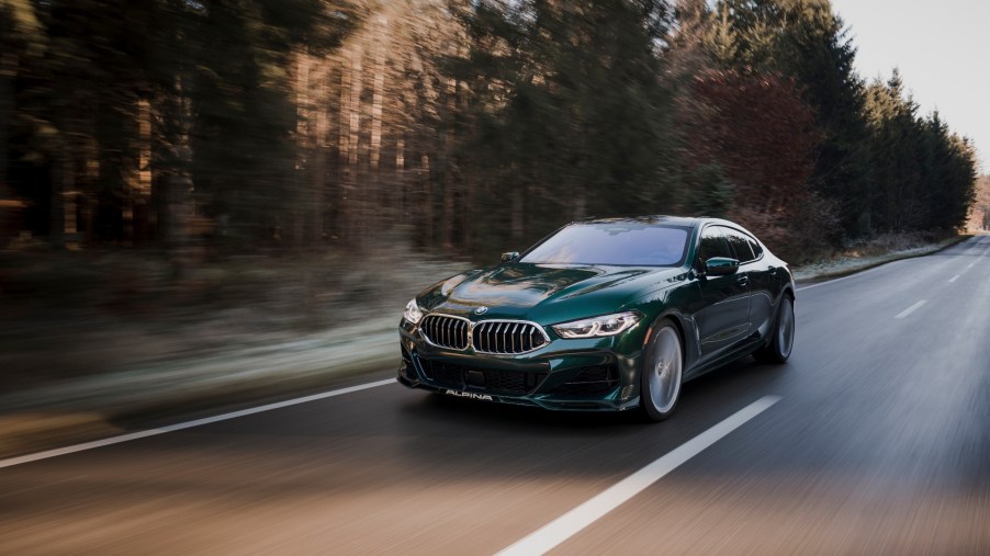A 3/4 front view of a green Alpina B8 sedan driving on a tree-lined road.