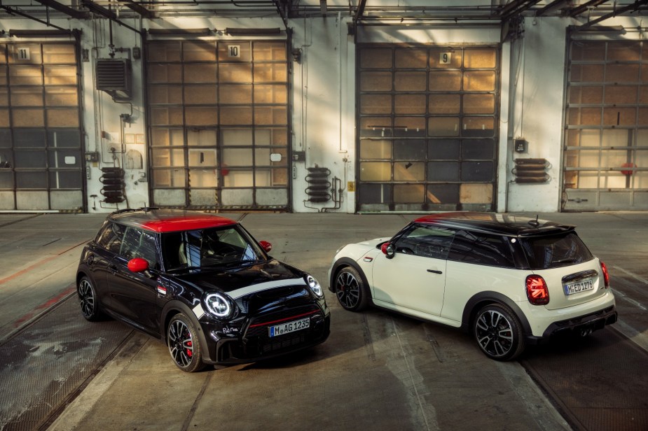 A view of a pair of MINI Pat Moss Edition Cooper JCW cars parked in a warehouse. A black car facing the camera and a white car facing away.