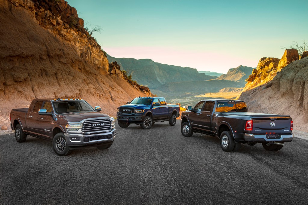 Three heavy-duty Ram pickup trucks parked on a road overlooking a desert valley.