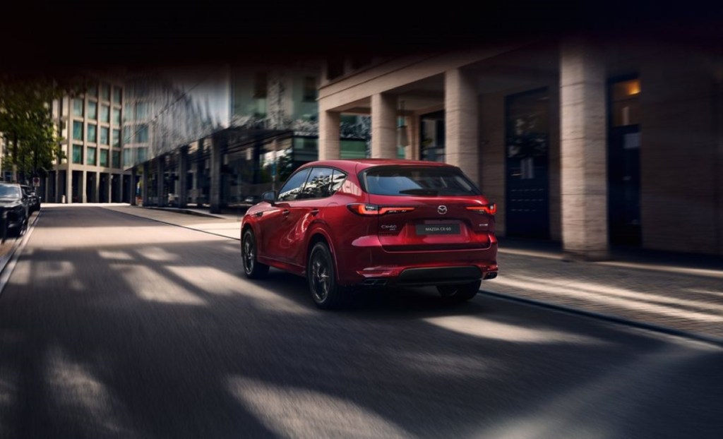 Red Mazda CX-60 driving by a large building, highlighting release date and price of 2023 Mazda CX-70
