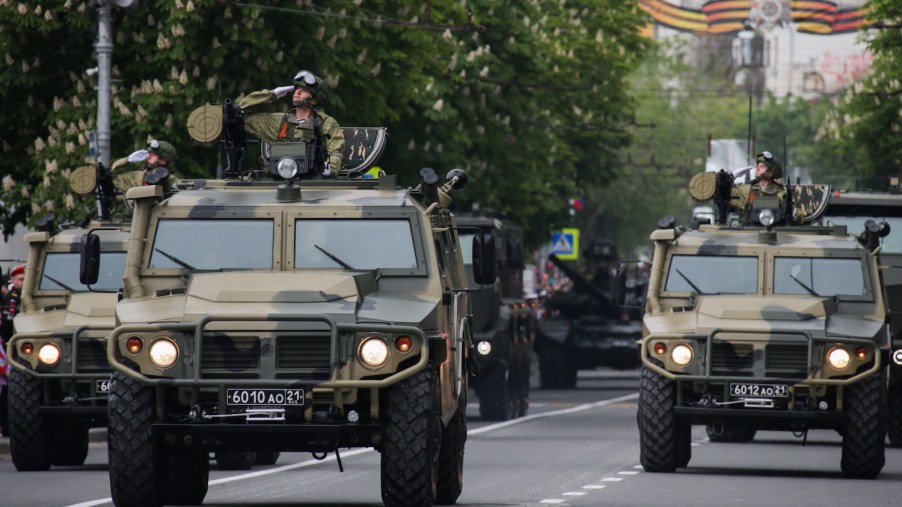 Cummins-powered Russian military vehicles parade through the streets of Crimea while a soldier salutes from the roof of each.