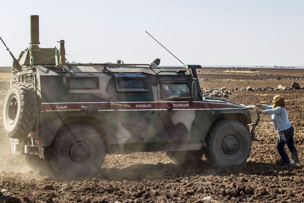 A Syrian civilian holds onto the grille of a Cummins-powered military vehicle, blocking its path through the desert.